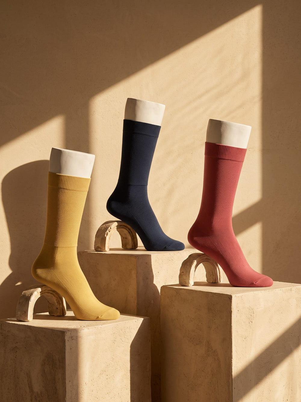 Mustard, navy and brick Silver Edition dress socks on white plaster legs, sandstone blocks in low sun
