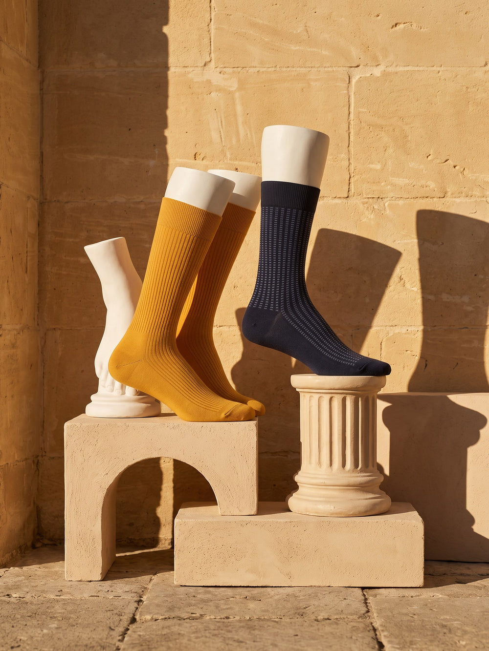 Ochre ribbed crew socks and a navy jacquard sock on white plaster legs beside a stone column
