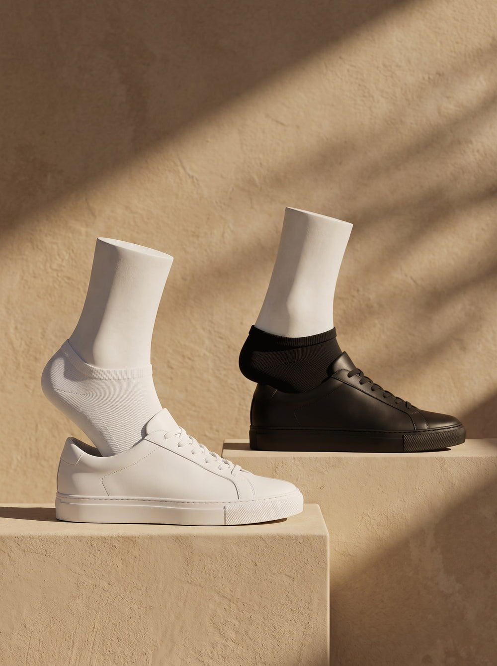 A white and a black Trainer Sock on white plaster feet in white and black leather trainers