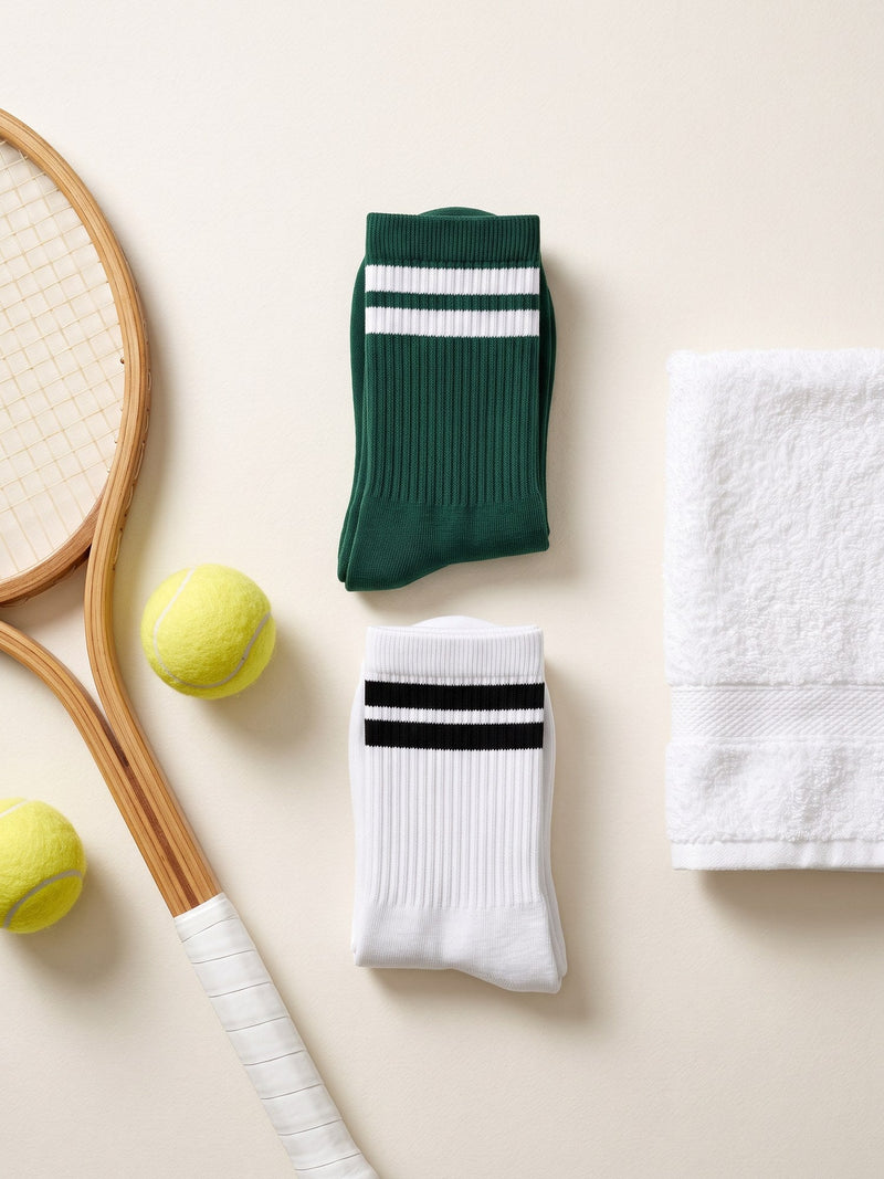 A green and a white Sport Sock with two-stripe cuffs beside a wooden tennis racket and tennis balls