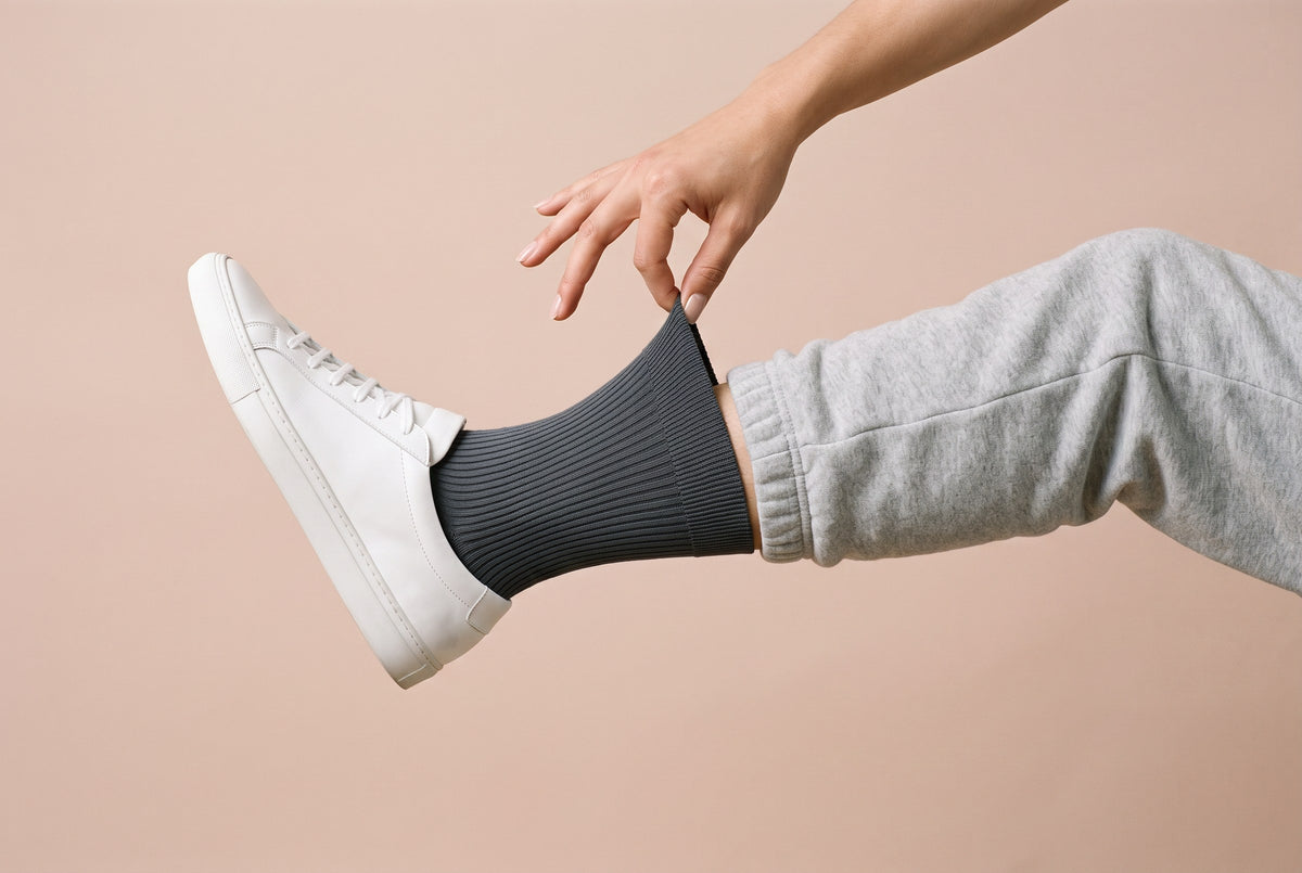 Charcoal ribbed crew socks being pulled up, with a white trainer and grey joggers