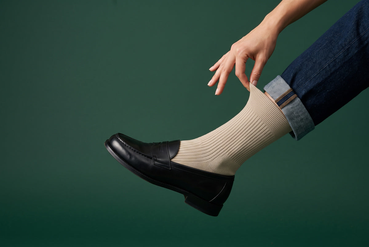 Sand ribbed crew socks being pulled up, with a black loafer