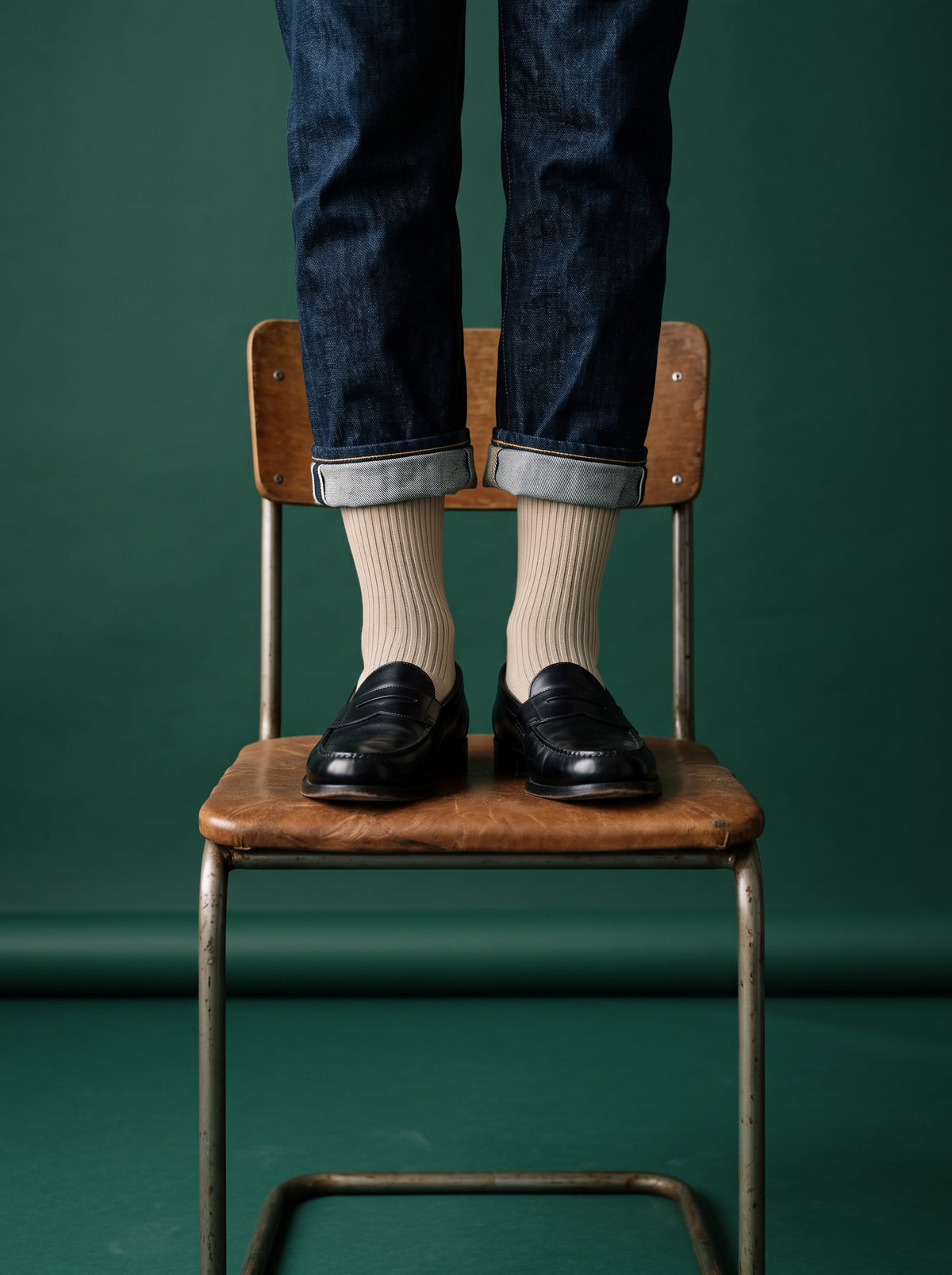 Sand ribbed crew socks with black loafers and jeans, standing on a wooden chair