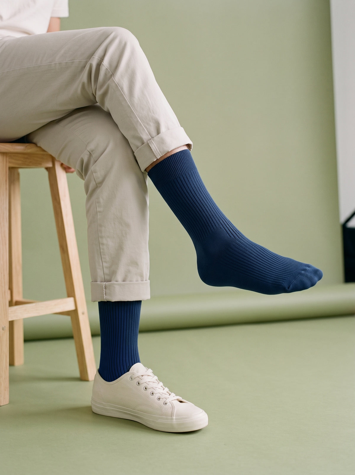 Navy ribbed crew socks worn with white trainers and stone chinos, legs crossed on a stool