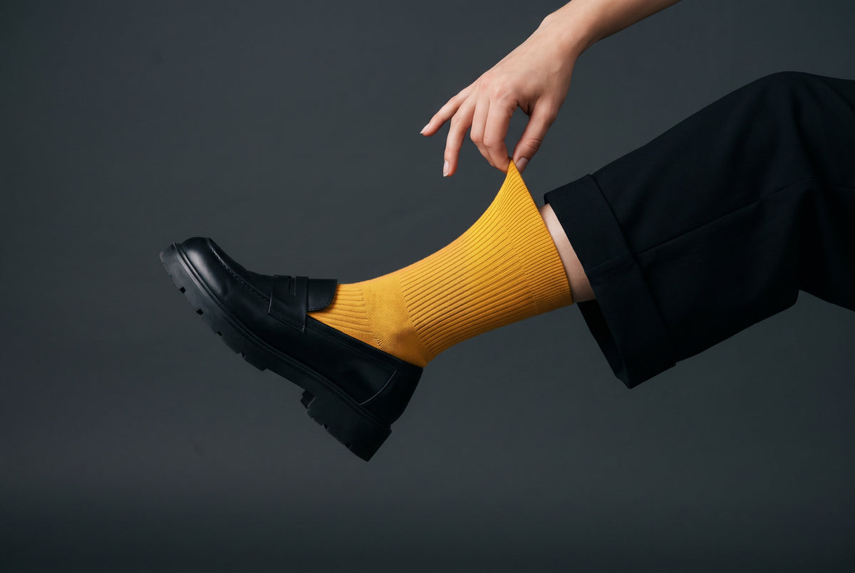 Ochre ribbed crew socks being pulled up, with a black loafer