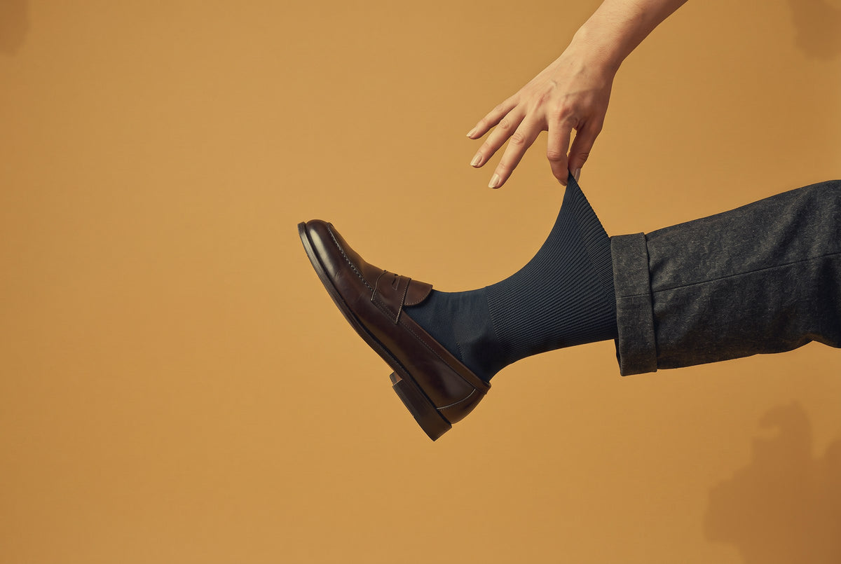 Navy Silver Edition dress socks being pulled up, with a brown loafer