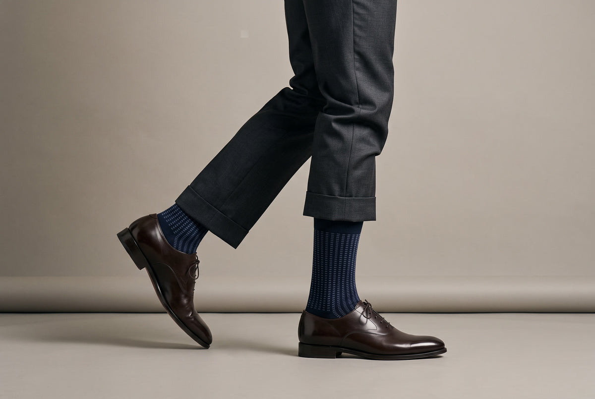 Navy jacquard crew socks mid-stride in brown shoes and grey trousers